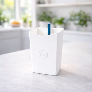 Weißer Behälter mit Logo und blauem Stift, helle Umgebung mit Pflanzen im Hintergrund